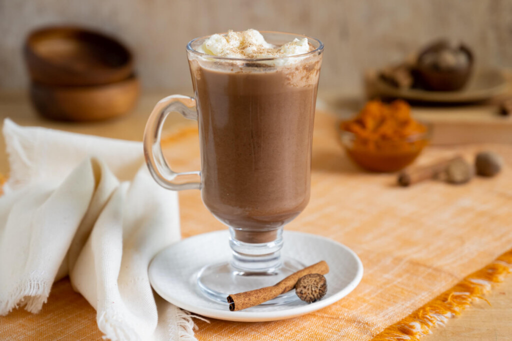 Glass mug of hot chocolate on a small plate.