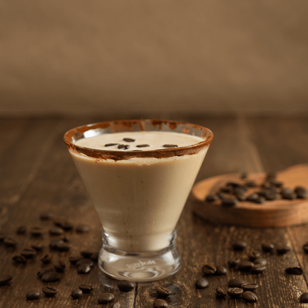 Cold brew martini mocktail with a cocoa-dusted rim and coffee beans on a wooden table surrounded by coffee beans.