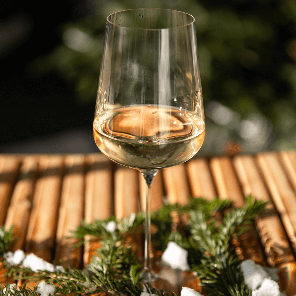 White wine glass on snowy winter table outdoors at vineyard with Christmas tree