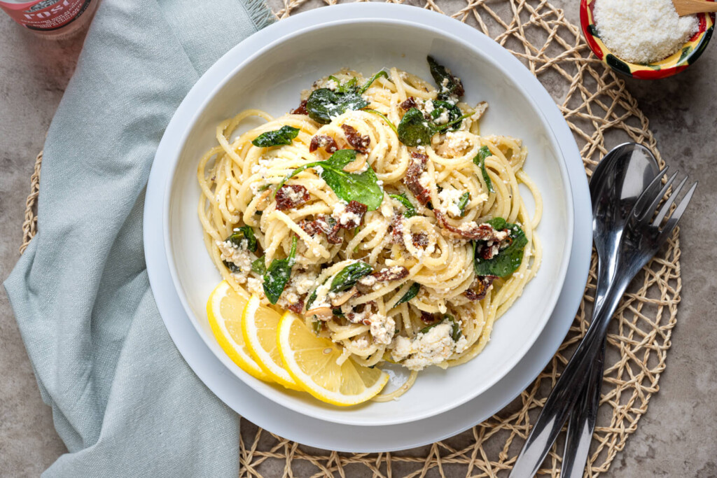 Overhead image of plate of spaghetti with sundried tomatoes, spinach, cheese, and lemon