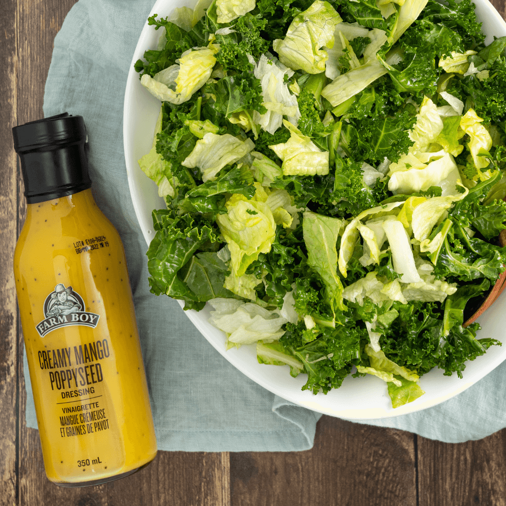 Overhead image of bowl of chopped lettuce greens beside bottle of Farm Boy Creamy Mango oppyseed Dressing